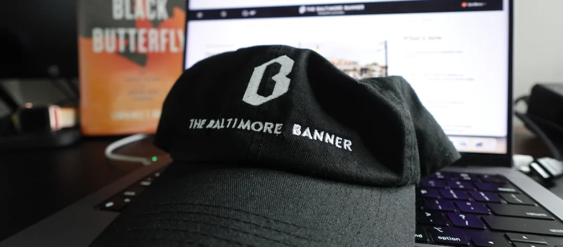 A picture of Baltimore Banner hat with a computer in the background and the book "The Black Butterfly."